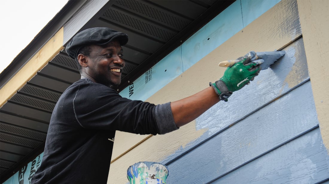 A volunteer smiling while painting a home.
